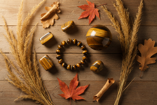 Tijgeroog collectie met armband, bol en tumble stenen op houten ondergrond met droge gouden grassen en herfstbladeren in warm gouden licht