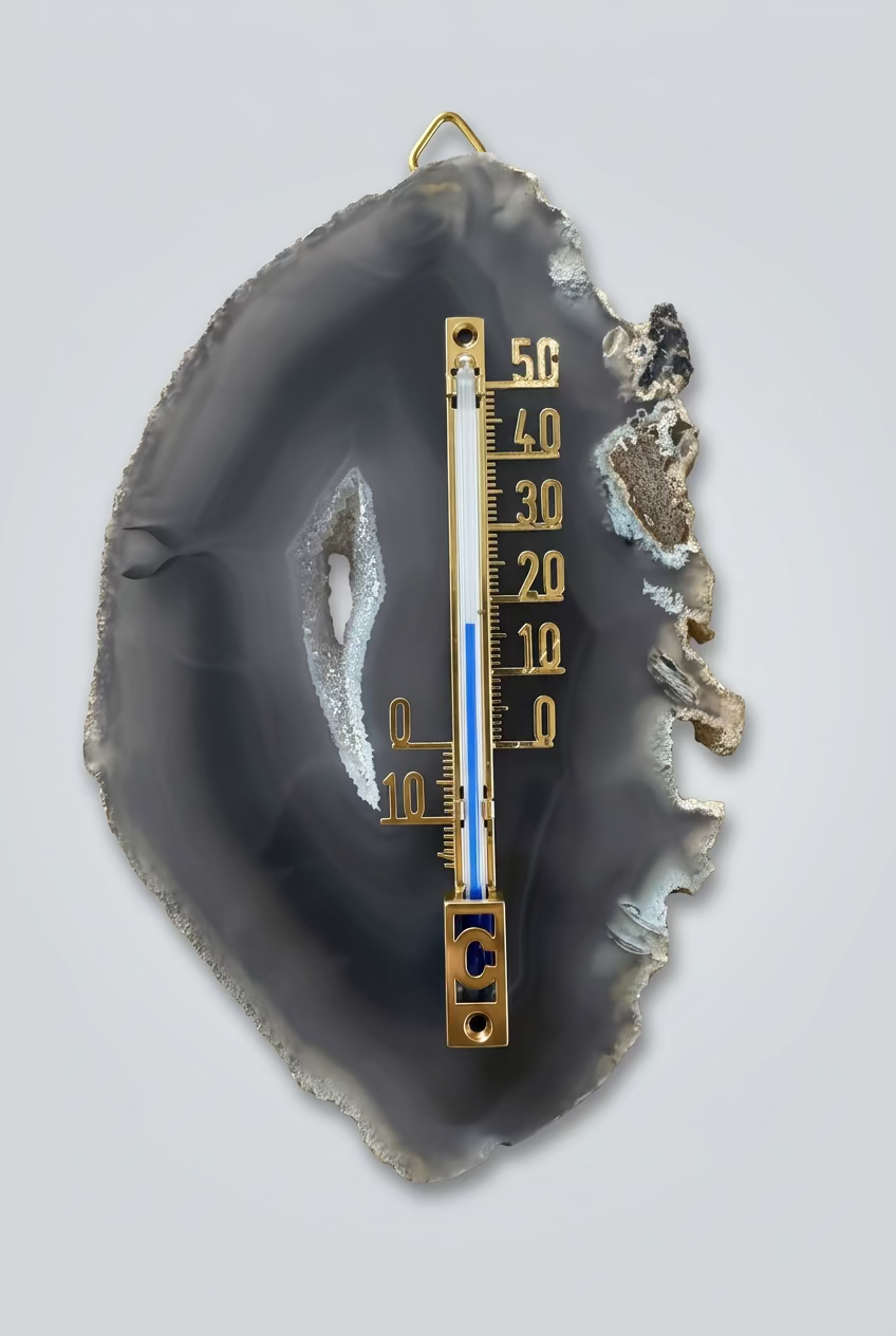 Agaatschijf met thermometer, donkergrijze banden, een lichte kristalrand rond de opening en een onregelmatige buitenrand