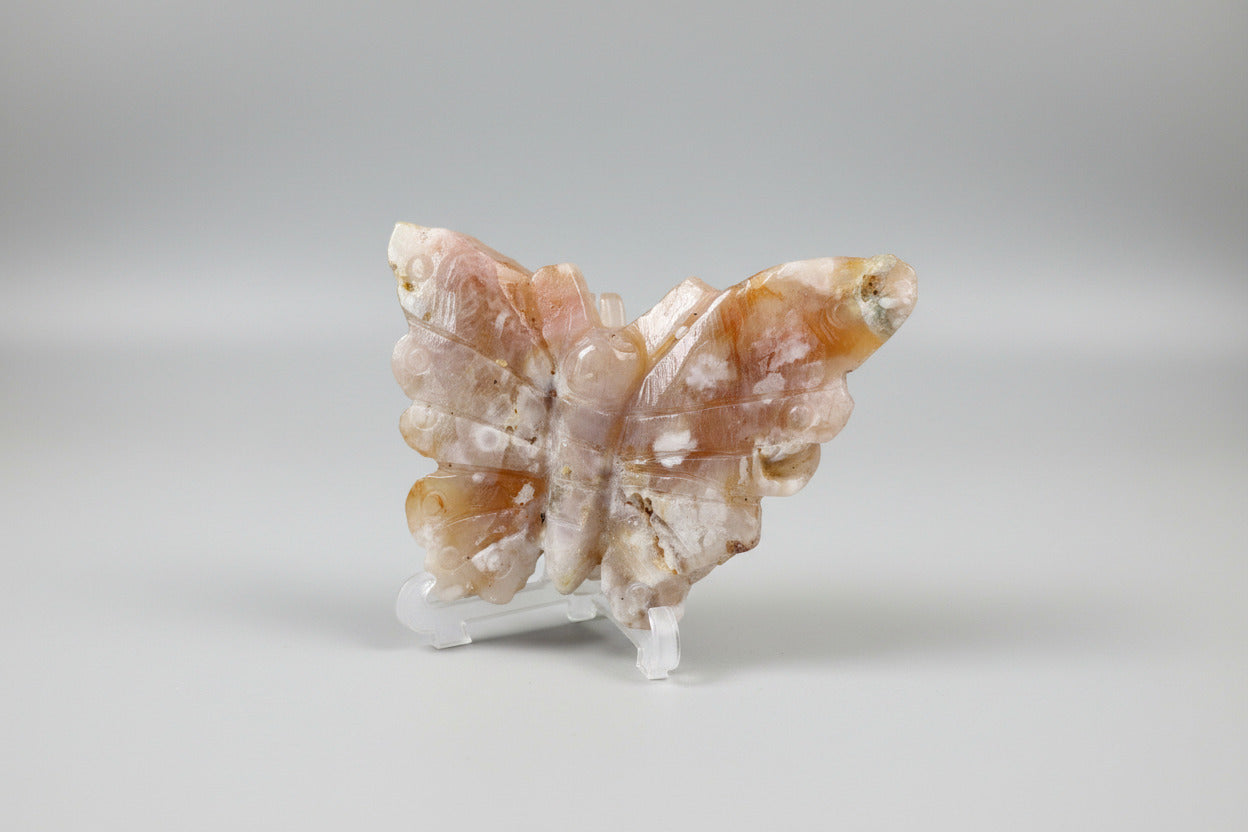 Handgesneden bloemagaat vlinder met zachte roze en oranje tinten op transparante standaard